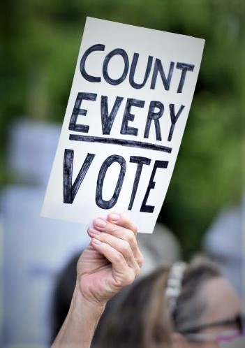 Hand holding sign reading "count every vote"